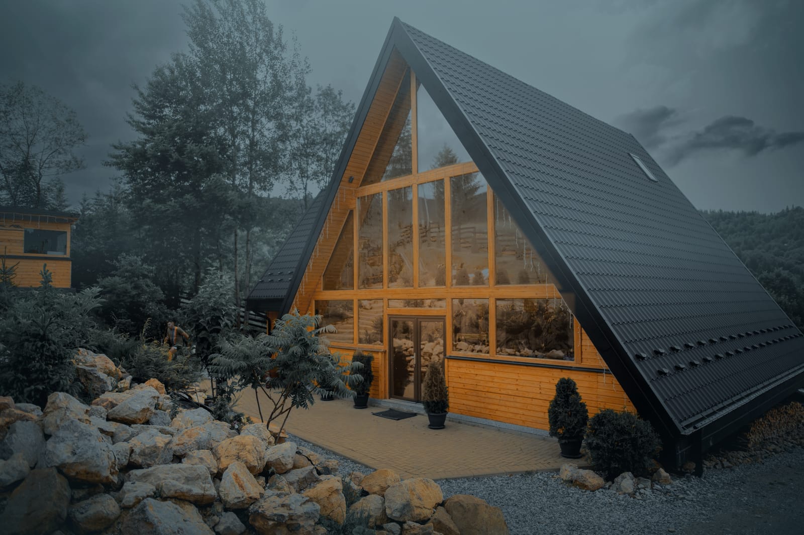 Green View Rarău A-Frame cabin at dusk, warm light in the glass gable, among fir trees and a rock garden